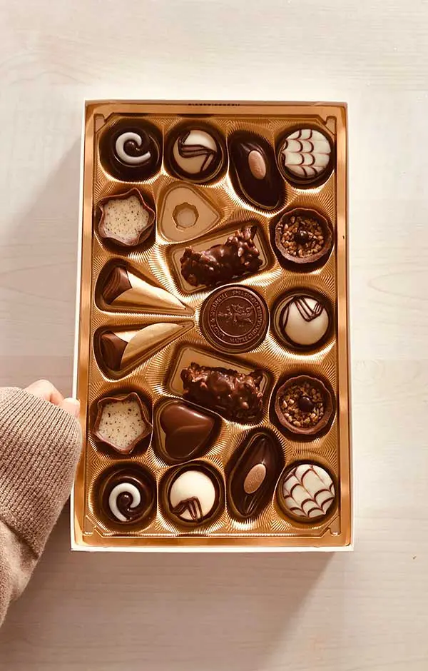 A box of chocolates with one hand holding it.